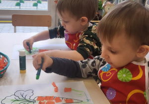 dzieci wykonuja pracę plastyczną klejąc pomarańczową bibułę