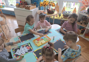 Dzieci siedzą przy stoliku i maja przed sobą tackę z kolorowymi kartonikami