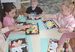 Dzieci przy stoliku naklejaja kolorowe kartoniki na liście