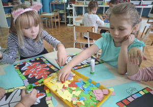 Dziewczynka wybiera czerwone karoniki do przyklejenia na swój liść dębu