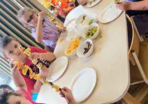 Dzieci przy stole pokazują owocowe szaszłyki