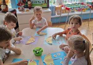 Dzieci siedzą przy stoliku z kartą pracy z parasolem