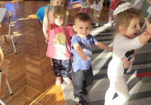 Dzieci idą po kole z rękami uniesionymi w gorze