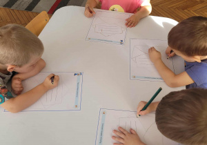 Dzieci przy stoliku kreślą znaki literopodobne