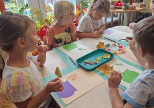Dzieci przy stoliku malują liście na barwy jesienne