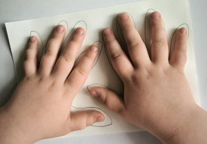 dzieczynka odrysowuje swoje dłonie, które będzie wycinać i przyklejać na talerzyk papierowy
