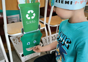 chłopiec segreguje odpady wkładając do zielonego pojemnika rysunek ze szklanym słoikiem