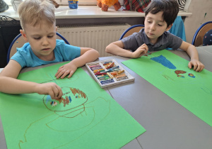 Chłopcy na zielonych kartonach malują strachy na wróble