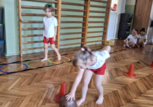 Dziewczynka toczy pilkę slalomem między pachołkami