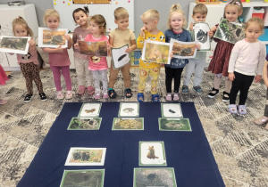 dzieci stoją trzymając plansze edukacyjne dot. tematu zwierzą w lesie
