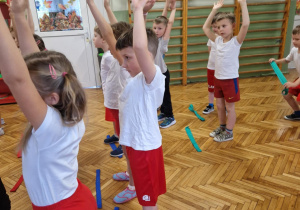Dzieci stoją z szarfami w rozsypce na sali gimnastycznej
