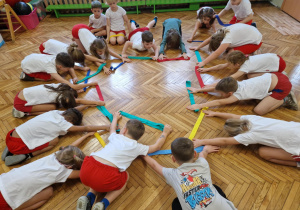 Dzieci leżą na brzuchu z rękoma, z szarfami uniesionymi w przód