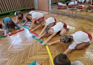 Dzieci robą skłon w przód z szarfami