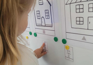 Dziewczynka przyczepia ilustrację do odpowiedniego domku