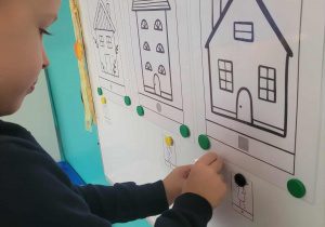 Chłopiec przyczepia ilustrację do domku z figura geometryczną kwadratu