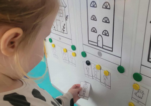 Dziewczynka przyczepia ilustrację do domku z figura geometryczną koła