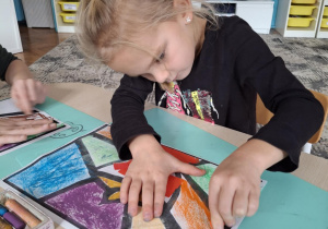 Dziewczynka maluje kawałek witrażu na pomarańczowo