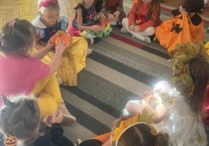 Dzieci w kole podają sobie z rąk do rąk dynie