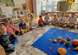 Dzieci siedzą przed różnymi rodzajami dyń