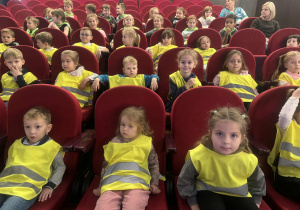 Dzieci siedzą na czerwonych krzesłach