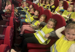 Dzieci siedzą w rzędach na sali teatralnej