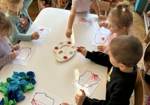 Dzieci przy stoliku malują czroną farbą