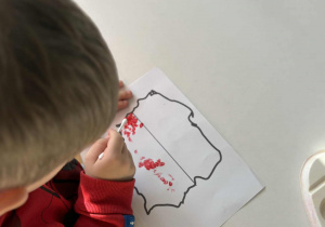 Cłopiec robi czerone kropki na mapie Polski