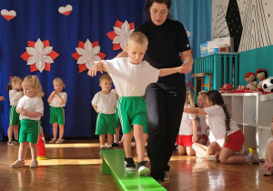Chłopiec przechodzi po ławeczce z asekuracją