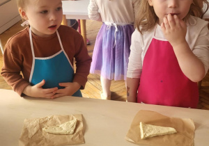 Dzieci stoja przy stole z trójkątnumi kawałkami ciasta