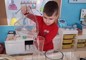 Chłopiec nalewa wodę do szklanego naczynia