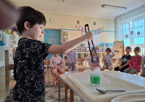 Chlopiec wkłada lód do szklanki z zieloną wodą