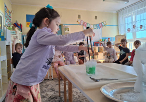 Dziewczynka wkłada lód do szklanki z zieloną wodą