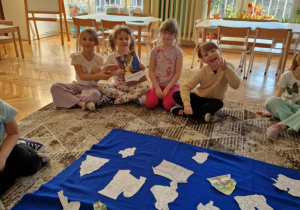 Dzieci siedzą na dywanie przed postaciami z bajek