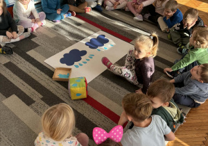 Dziewczynka siedzi przed chmurami z kartonu