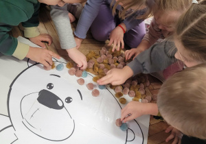 Dzieci wyklejają puszkami głowę misia