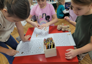 Dziewczynki rozwiązuja kartę pracy z labiryntem