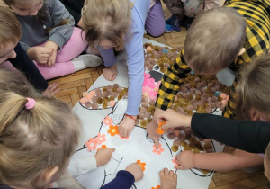 Dzieci naklejają puszki na sylwetę misia