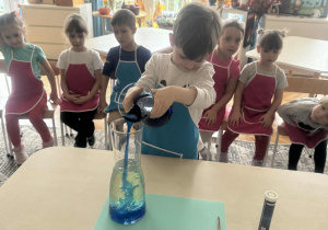 Chłopoiec przelewa wode z barwnikiem do innej menzurki