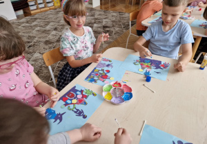 Dzieci siedzą przy stole z paleta farb