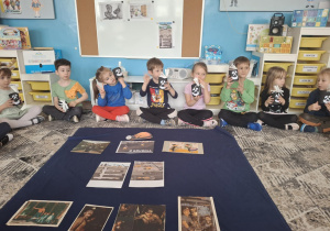 Dzieci siedza na dywanie przed planszam z gónikiem