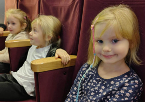 Dziewczynki siedzą na krzesłach w sali kinowej