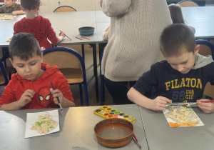 Chłopcy malują przy stole aniołki farbami