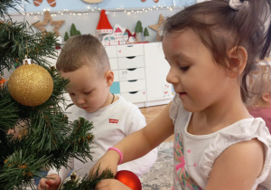 Dziewczynka zakłada złota bombkę na galązkę choinkową