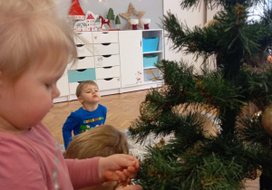 Dziewczynka zakłada bombkę na gałązkę choinkową