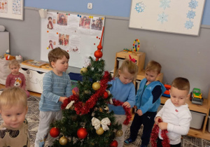 Dzieci oplatają łańcuhcem choinkę