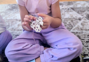 Dziewczynka nawleka sznurek na drewnianego aniołka