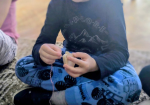 Chłopiec nawleka sznurek na drewnianego buta