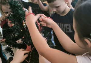 Dzieci oplatają łańcuchem choinkę