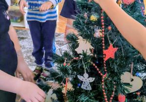 Dzieci nakładają łańcuch z koralików na choinkę