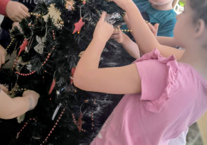 Dzieci nakładają złoty łańcuch na choinkę